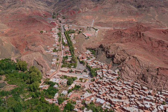 Aerial view of the ancient village nestled within the red hued mountains, with traditional red mud brick houses and lush greenery, Abyaneh, Isfahan Province, Iran.