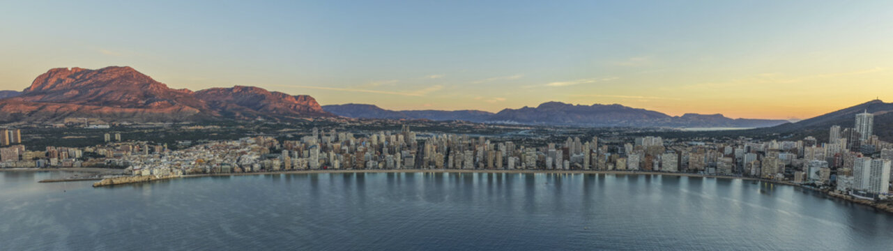Aerial view of the sun kissing the towering skyscrapers along the Playa de Levante, with the rugged Sierra Helada mountains in the background, Benidorm, Valencian Community, Spain.