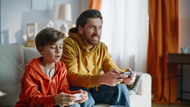 Father son playing video game sitting sofa closeup. Happy man boy rejoicing 