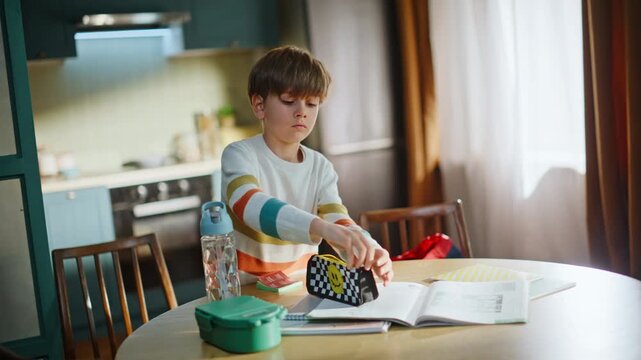 Boy packing school backpack home kitchen. Serious preteen child organizing
