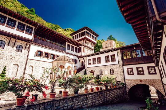 View of the vibrant terracotta flowers lining the stone walls of the Monastery of Saint John the Baptist under a clear blue sky, Mavrovo, North Macedonia.