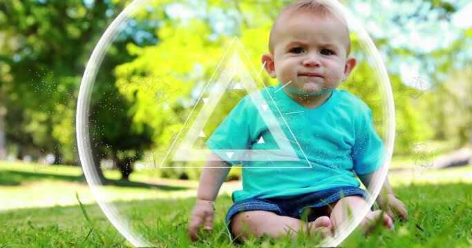 Sitting baby wearing teal shirt, shorts on green grass in park, showing ring and triangle overlays