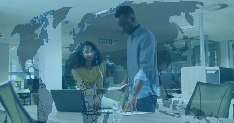 Leaning colleagues in yellow and blue shirts reviewing laptop and papers in office, map overlay