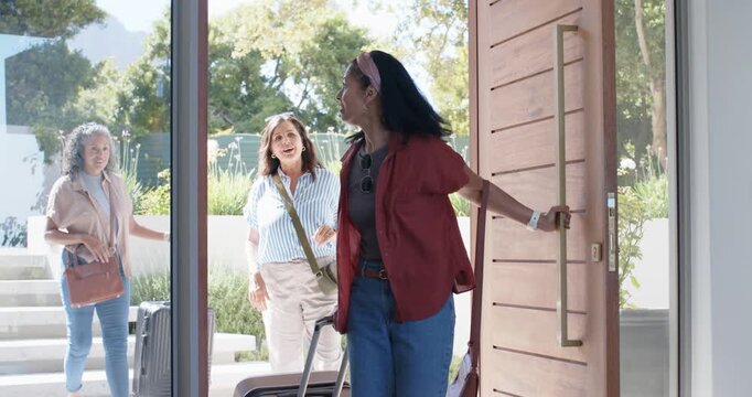 Three women with suitcases arriving at front steps lead woman opening wood door to inspect interior