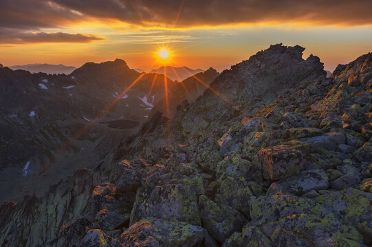 View of the sun bursting through the peaks, casting a golden glow on the rugged, moss-covered rocks in the mountains, Vysoke Tatry, Presov Region, Slovakia.