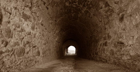 Obraz premium Dark stone tunnel opening to a bright, snowy winter landscape Long, dark, arched corridor with light at the end, ancient and mysterious Dark stone tunnel leading to light