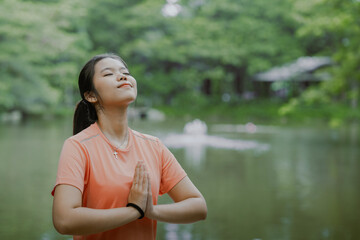 Young asian woman practicing yoga in forest near stream of water or river. Beautiful female doing yoga and meditation on nature. Health and mental well-being. Closeness of people to nature concept.