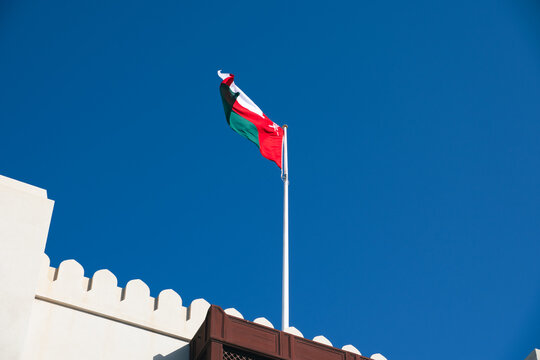 Oman national flag waving against clear blue sky above traditional Governate building in Muscat, the sultanate of Oman

