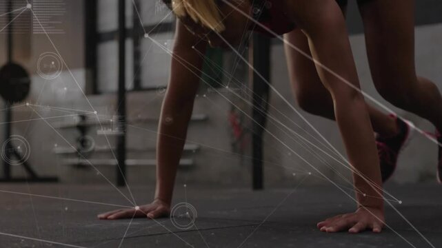 Performing mid-adult woman wearing red top moving push-up into tuck jump at gym with HUD overlay