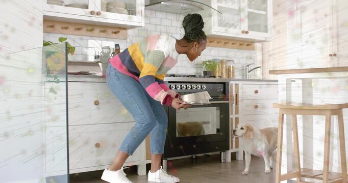 Holding baking pan, woman in striped sweater, jeans crouching in kitchen, offering stainless bowls