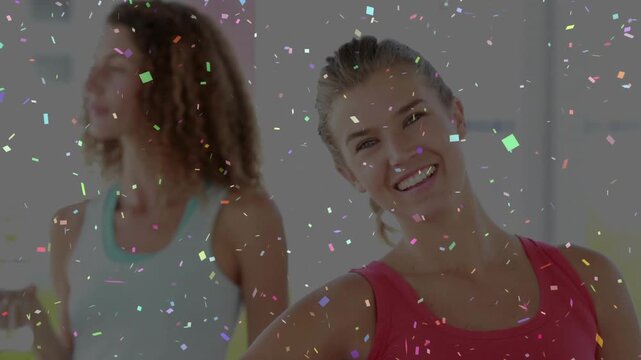 Carrying woman in red tank top positioning blue mat in bright fitness studio, confetti floating