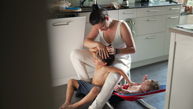 Mother checking older child&rsquo;s hair for lice while baby relaxes in rocker, everyday parenting, hygiene care, real-life motherhood, balancing responsibilities, attentive caregiving