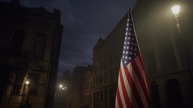 American flag waving on a lamppost in a deserted city street at night with buildings in the background, possibly for a patriotic or national event