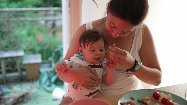 Mother feeding baby first solid food, baby biting vegetable, early food exploration, baby-led weaning, sensory development, introduction to new flavors, learning to eat