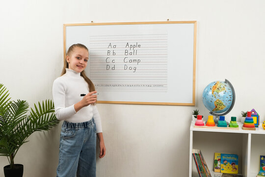 High-quality shot of a young female student practicing spelling at the blackboard. Capturing childhood education, literacy development, and academic success in a primary school.