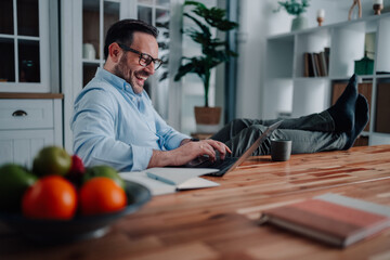 Man working remotely from home, laughing and relaxing with feet up on the desk, enjoying a...