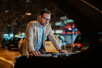 Man encountering trouble with his automobile, checking engine under the open hood, using smartphone...