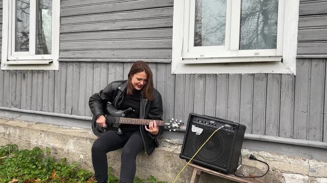 female rock musician in a leather jacket plays an electric guitar with an amplifier