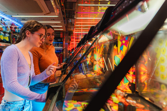Young women friends enjoying time together, playing arcade games at a fair at night