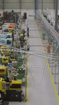 Vertical video: Worker appearing from far end and walking manufacturing aisle, inspecting stations