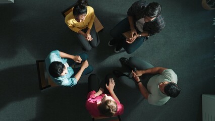 Top down aerial view of diverse business people hold wrist while sitting circle together. Faithful...