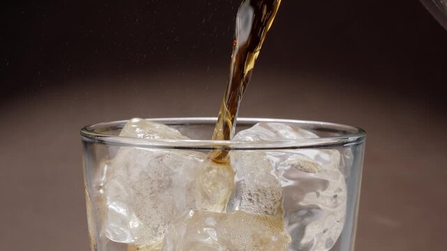 Close-up shot of cola being poured into a glass on the table with visible foam, fizz and rising carbonate bubble.