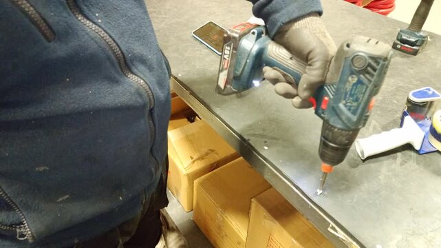 Worker using a cordless drill to screw a linoleum sheet onto a workbench during furniture or workshop installation work.
