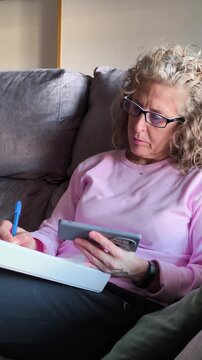 Woman using smartphone while writting on sofa