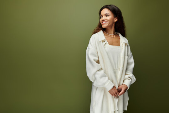 Beautiful young woman smiling gracefully in a cozy white outfit against a soothing green backdrop
