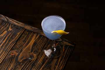 Bright blue cocktail sits on wooden table with a lemon twist during an evening gathering in a cozy bar setting © Serega