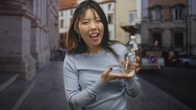 Woman holding a water bottle with hand presenting palm up and smiling gesture on a street; playful curiosity.