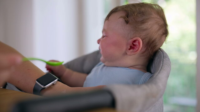 Baby reacting with teary eyes while being fed, resisting spoonful of food, showing discomfort, strong emotional response, early childhood feeding challenge
