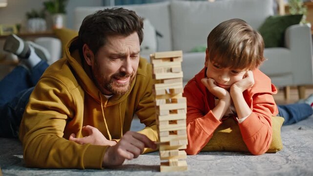 Man pulling jenga block ruining wooden tower feeling frustration home closeup.