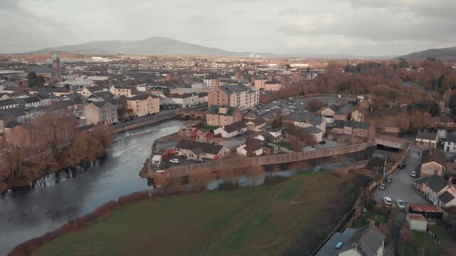Aerial drone gliding over historic Clonmel town and River Suir, revealing Irish architecture and distant mountains under overcast sky.