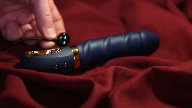 A man plugs a dildo into a charger. The sex toy lies on a red cloth.
