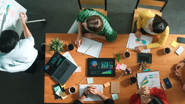Top view of smart business man standing while writing and presenting marketing idea at whiteboard. Group of diverse happy people looking at stock market chart and listening presentation. Convocation.
