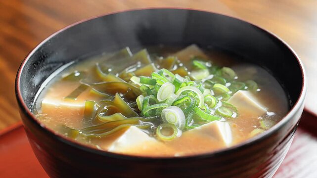 Close up of miso soup in a dark bowl with tofu seaweed and green onions