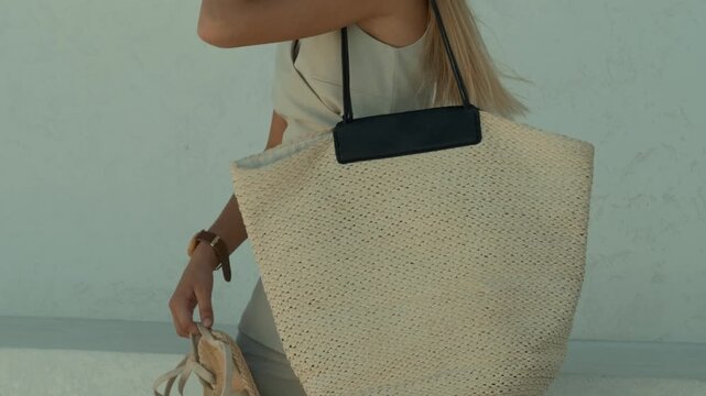 Woman in light linen outfit carrying a large woven straw tote bag
