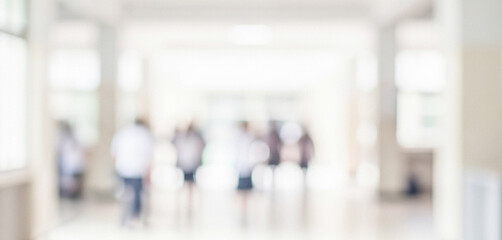 Fototapeta premium A blurred image of people walking in a brightly lit hallway. The soft focus creates a sense of movement and activity in a modern building setting.