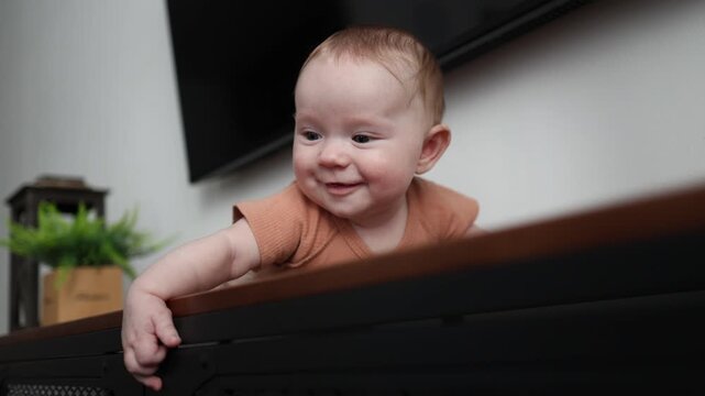 Close-up of a smiling infant on a cabinet, looking sideways and drooling heavily