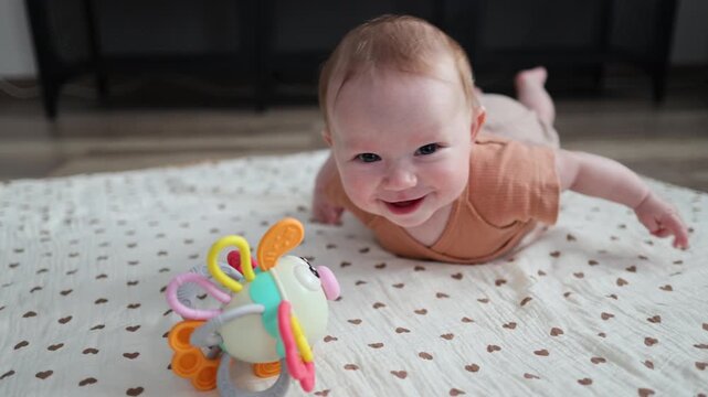 Happy baby on a mat reaching for a colorful toy, smiling and laughing during tummy time.