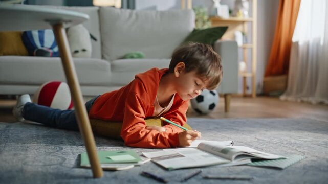 Elementary school student studying home lying floor closeup. Boy pupil writing