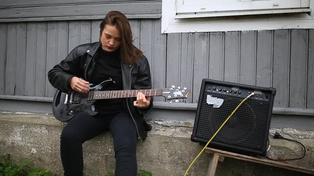 female rock musician in a leather jacket plays an electric guitar with an amplifier