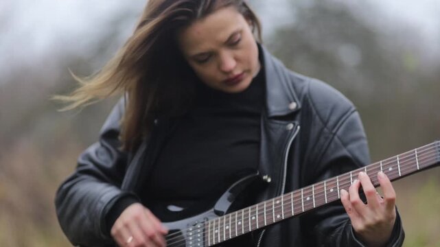 Young woman in a leather jacket, rock musician plays electric guitar outdoors