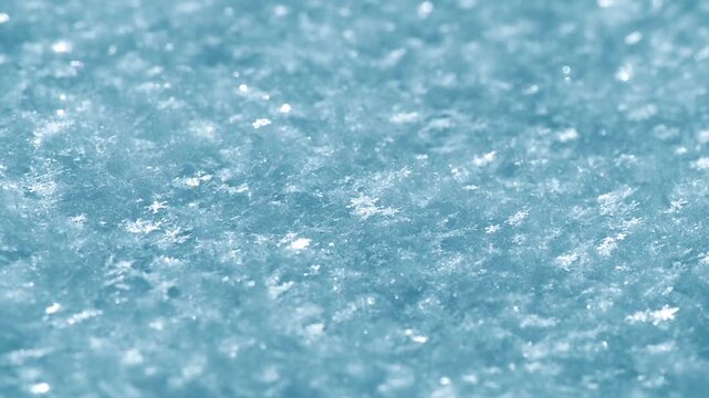 Snow surface showing many individual ice crystals and fine granular flakes creating a textured light blue winter pattern with glimmering highlights, ideal for seasonal backdrops