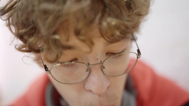 Extreme close-up of a young man with curly hair and glasses sipping a drink through a white straw. He is focused on his beverage, with a shallow depth of field blurring the background.