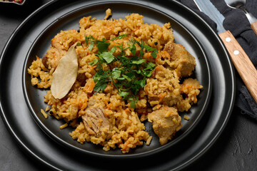 Pilaf with rice and pieces of meat in a black round plate on the table, delicious food