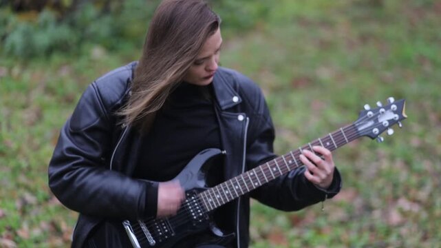 Young woman in a leather jacket, rock musician plays electric guitar outdoors