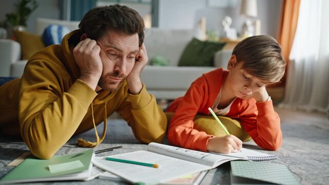 Tired father support study little son writing homework lying floor closeup.