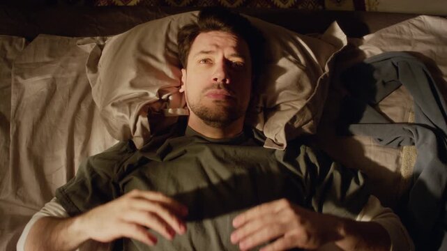 Top view shot of middle aged man with beard lying on bed holding head in frustration while feeling anxious getting up in morning